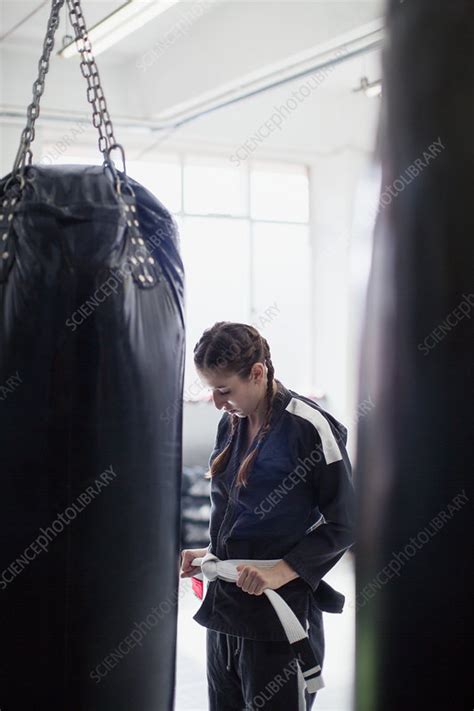 Young woman tying jiu-jitsu belt next to punching bag - Stock Image ...