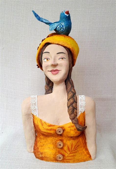 a ceramic statue of a woman with a bird on top of her head, wearing a ...