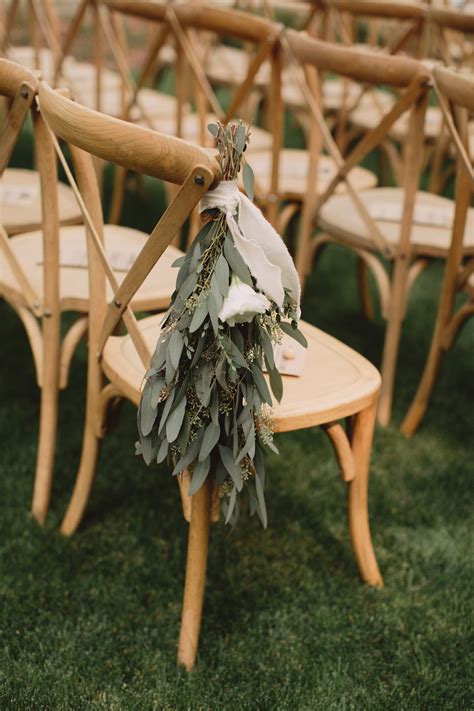 Seeded eucalyptus, beige ribbon, wooden cross-back chairs, ceremony ...