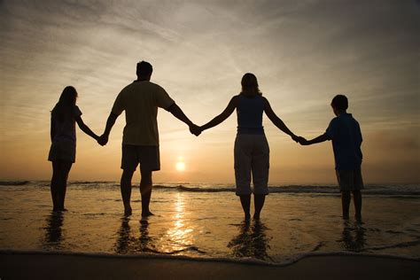 Silhouette of family holding hands on beach watching the sunset. Horizontally framed shot ...