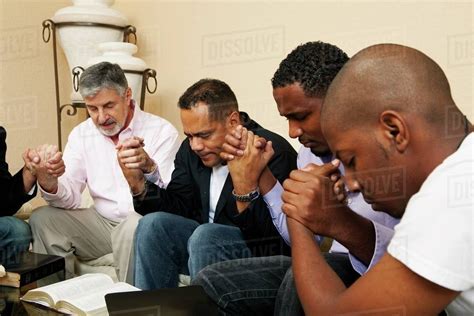 A Group Of Men Praying Together With An Open Bible - Stock Photo - Dissolve