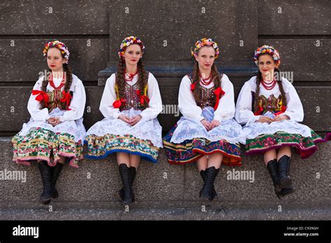 Poland, Cracow. Polish girls in traditional dress sitting at the base ...