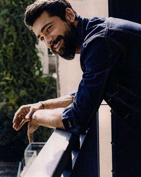 a man with a beard leaning on a balcony rail and looking at the camera while smiling