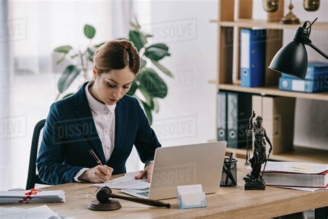 Female lawyer in suit at workplace with laptop, gavel and Femida in ...