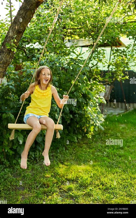 Happy barefoot laughing child girl swinging on a swing in sunset summer day on the backyard at ...