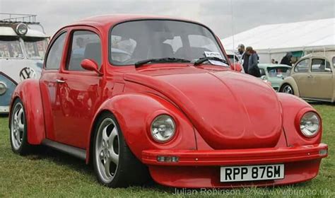 a red vw bug parked on top of a grass covered field next to other cars