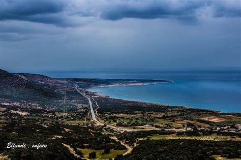 an aerial view of a road near the ocean under a dark sky with storm clouds