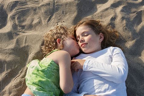 Two Sisters Lying On The Beach Kissing On The Cheek | Stocksy United