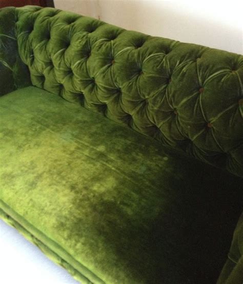 a green velvet couch sitting on top of a hard wood floor next to a white wall