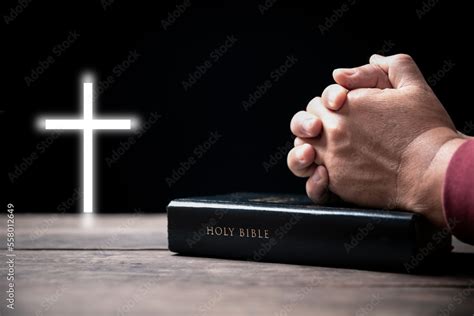 Hands folded in prayer on Holy Bible with cross in church concept for ...