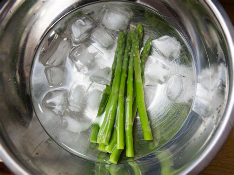 asparagus in ice cubes on top of a metal bowl filled with water