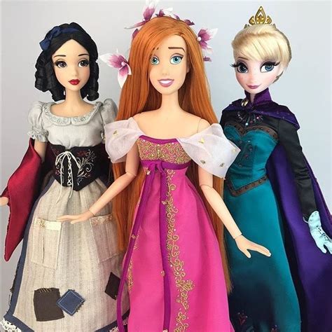 three dolls are standing next to each other wearing dresses and tiaras, one is holding a cell phone