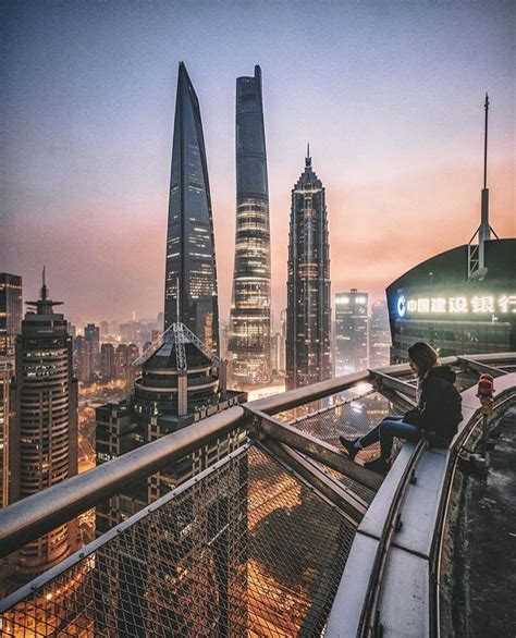 a man sitting on top of a metal railing next to tall buildings in the city