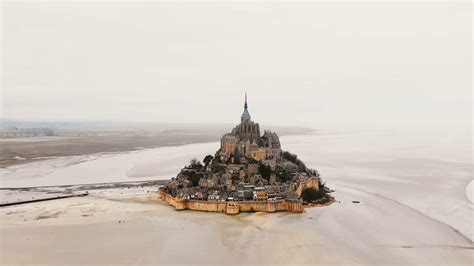 Drone flying left high above iconic Mont Saint Michel island and abbey, epic famous travel ...