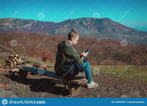 A Young Guy Dressed for Hiking Sits High in the Mountains and Looks a Mobile Phone Stock Image ...