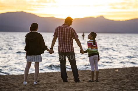 A father holds hands with his daughters while they watch the sunset on ...