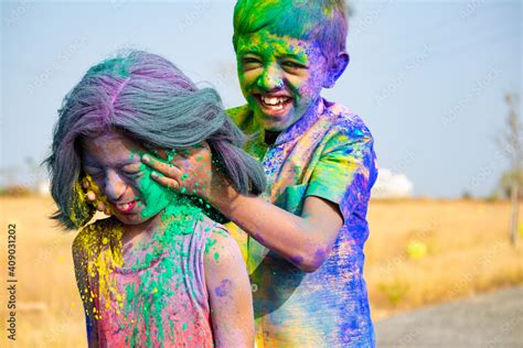 Young kid from the back applying holi colors to girls face during holi festival celebration ...