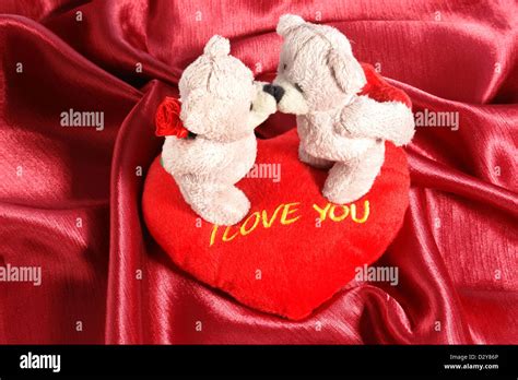 Two stuffed teddy bears kissing each other on stuffed heart-shaped ...