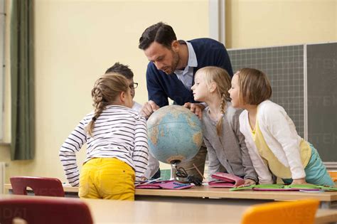 Teacher and pupils looking at globe in classroom stock photo