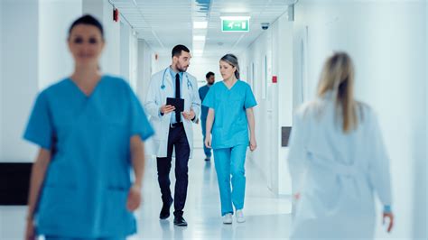 Surgeon and Female Doctor Walk Through Hospital Hallway, They Consult Digital Tablet Computer ...