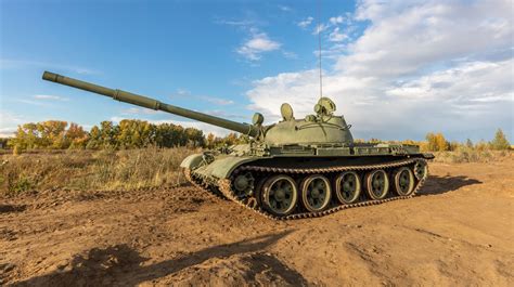 A side shot of old russian tank T-62 in the field. Blue cloudy sky as a ...