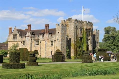 people are walking around in front of a castle like building with hedges on the lawn