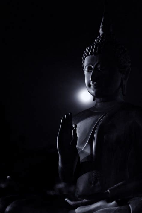 a buddha statue sitting in the dark with its hands clasped up to it's chest