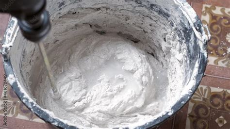 A person mixes cement and water in a container to get the finished mixture. The construction ...