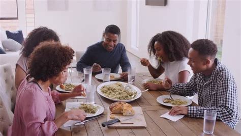 Elevated view of happy black family sitting at dinner table eating together and talking - Stock ...