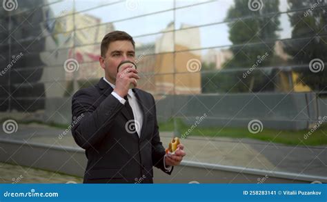 Young Businessman Eats Fast Food. a Man in a Suit Walks Next To the Business Center Drinking ...