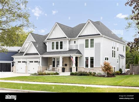 A new, white and grey modern farmhouse with a grey roof and two car ...