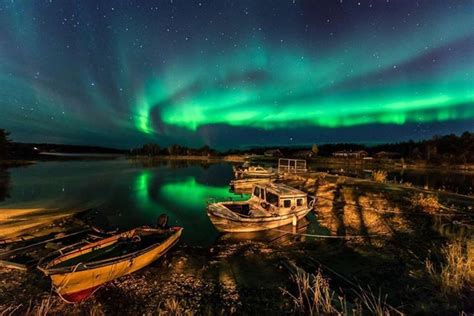 two boats are sitting on the shore under an auroral sky with green and ...