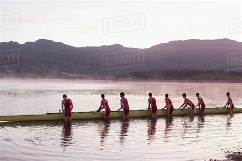 Rowing crew placing scull in lake at dawn - Stock Photo - Dissolve