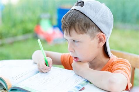 Premium Photo | A boy in a cap solves math examples at a table on the street child doing ...