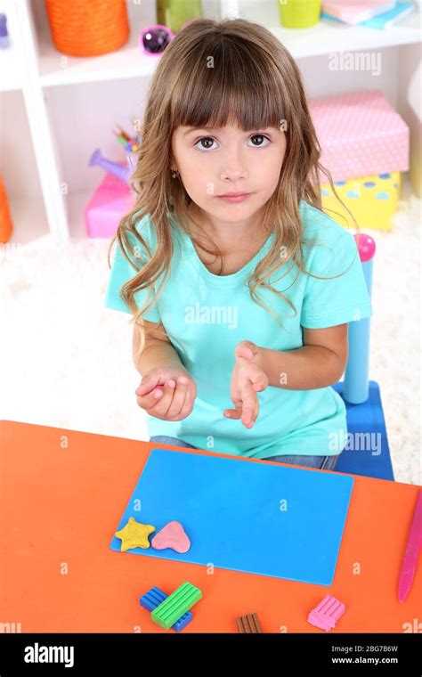 Little girl molds from plasticine sitting at table in room on shelves background Stock Photo - Alamy