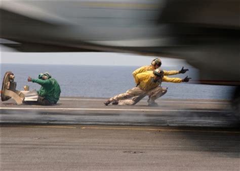 An F/A-18 Hornet accelerates past flight deck shooters