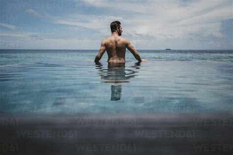 Rear view of man relaxing in infinity pool, Maguhdhuvaa Island, Gaafu ...