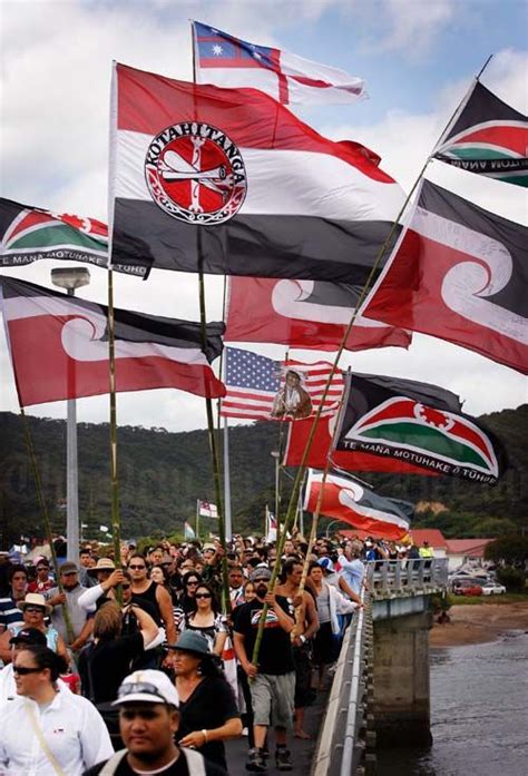 A large number of Māori flags are being flown as a large group crosses ...