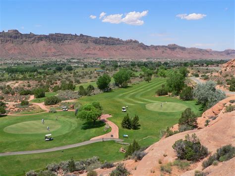 a golf course in the desert with mountains in the background and people playing on the green