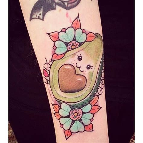 an avocado tattoo on the arm with a bat above it and flowers around it