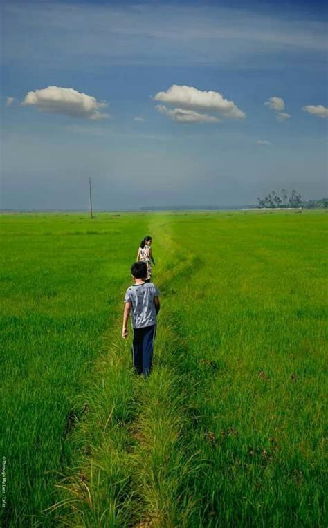 two people walking in the middle of a green field with blue sky and ...