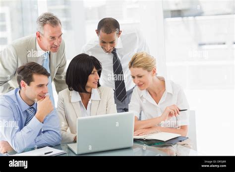 Happy business people gathered around laptop talking Stock Photo - Alamy