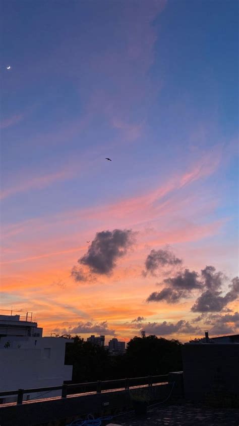 an airplane flying in the sky at sunset with clouds and buildings ...