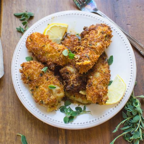 some fried food on a white plate with lemon wedges and herbs next to it