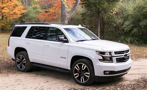 a white suv parked on top of a dirt road in front of trees and leaves