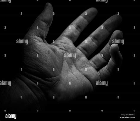 A grayscale shot of a human hand reaching out toward an unknown entity against a black ...