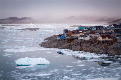 Small icebergs from the Ilulissat Icefjord floating along the coastline of colourful houses in ...