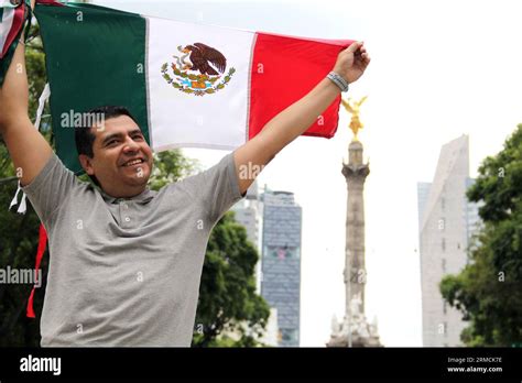 A dark-haired adult Mexican proudly raises the tricolor flag in Mexico City to celebrate his ...