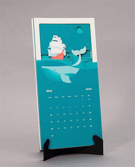 a desk calendar with an image of a boat and whale on the water, in front of a gray background