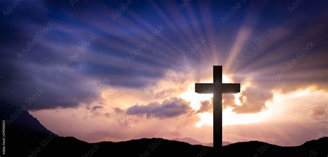 Jesus Christ cross on an amazing mountain sunset background with dramatic lighting and sunbeams ...